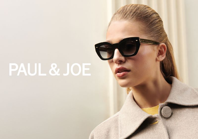A blonde woman wearing sunglasses and a tan jacket is featured in a fashion product shot with the PAUL & JOE logo.