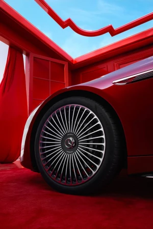 Close-up of a modern red car showcasing a detailed wheel, set in a matching red interior with a blue sky visible through a window.