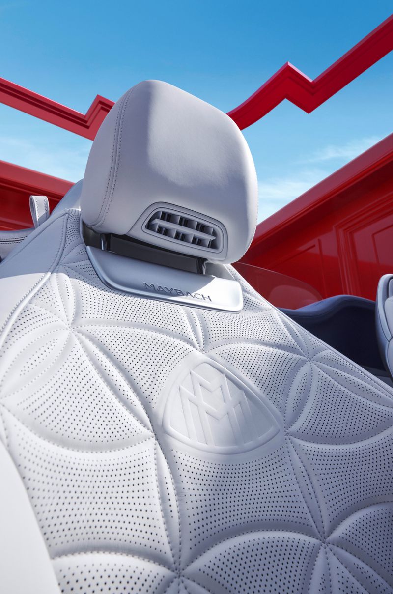 Luxury car interior featuring white leather seats with a quilted pattern, accented by the Maybach logo, set against a bright blue sky.