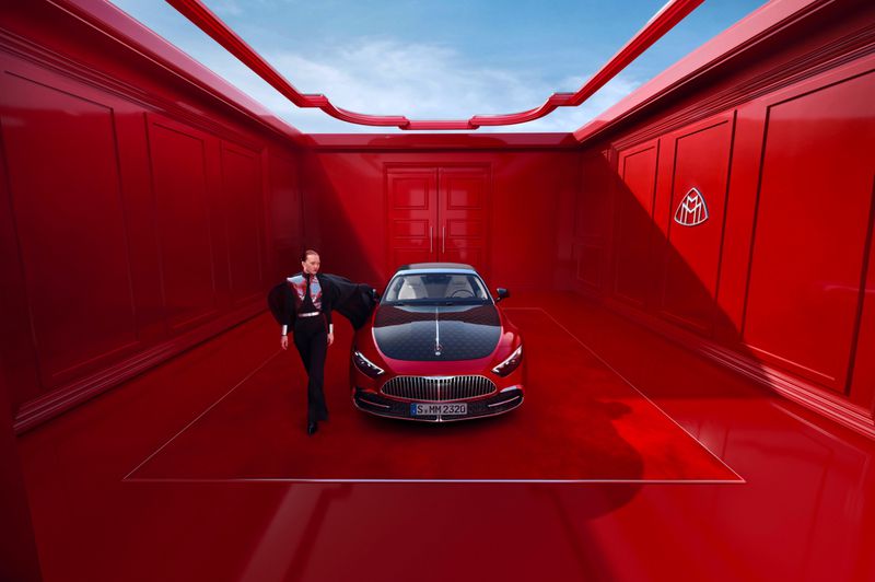 Red Maybach car showcased in a monochromatic red studio setting with a person in avant-garde attire standing alongside the vehicle.
