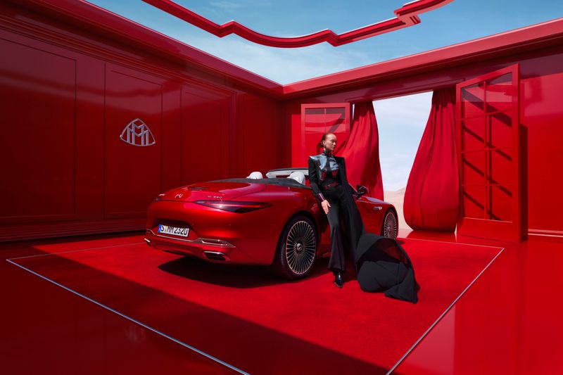 Elegant convertible parked indoors with an adult female model wearing a sophisticated black outfit, set against a monochromatic red backdrop.