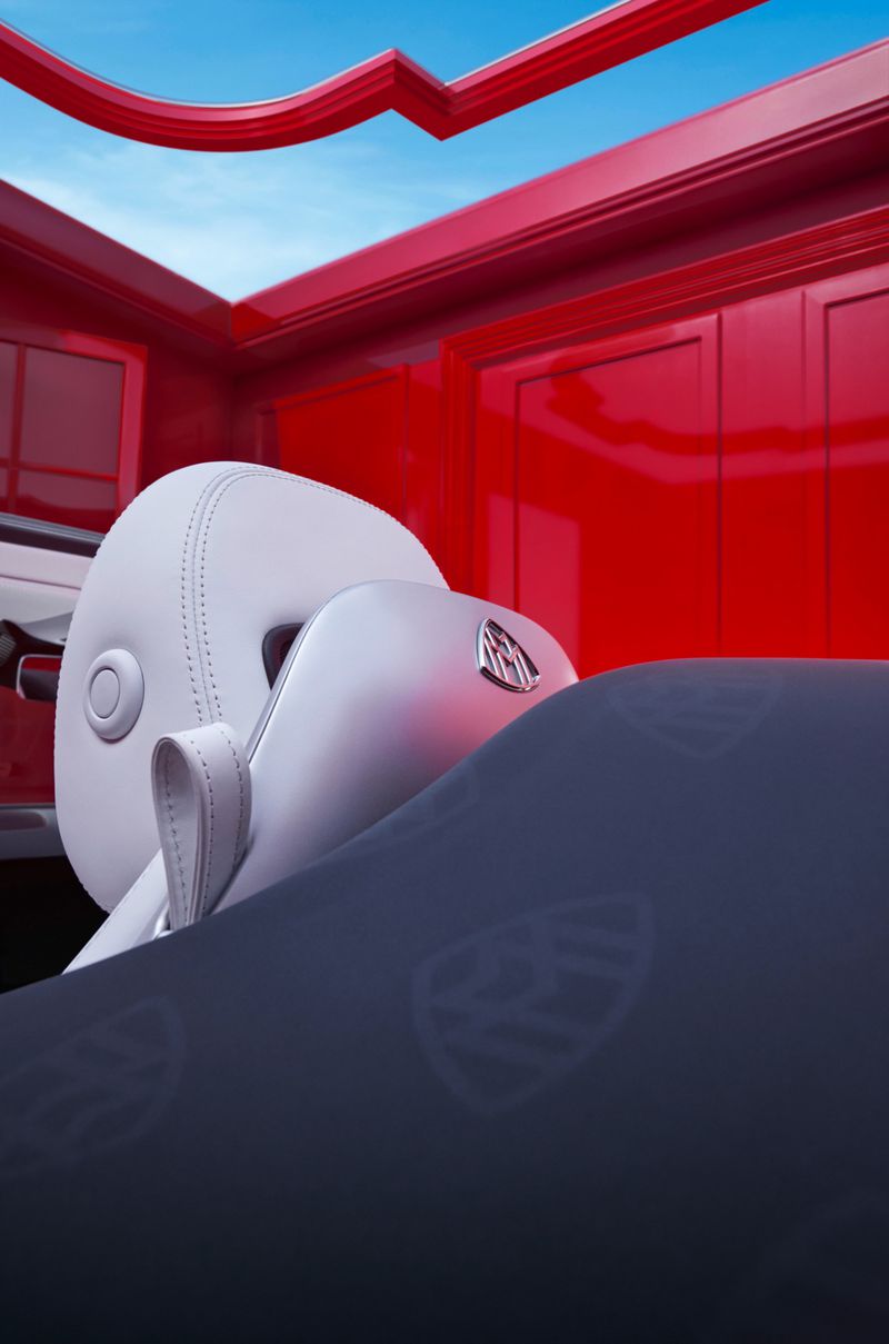 Interior view of a car with white seats and a dark blue blanket with a repeating pattern, set against a red interior and blue sky.