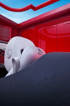 Interior view of a car with white seats and a dark blue blanket with a repeating pattern, set against a red interior and blue sky.