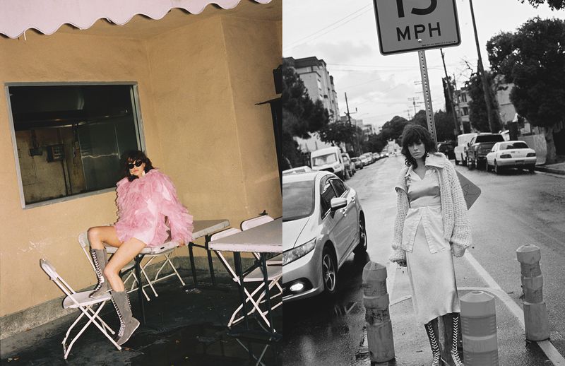 Fashion shot showcasing a woman in a pink ruffled jacket sitting on a chair with another woman in a white outfit on a city street.