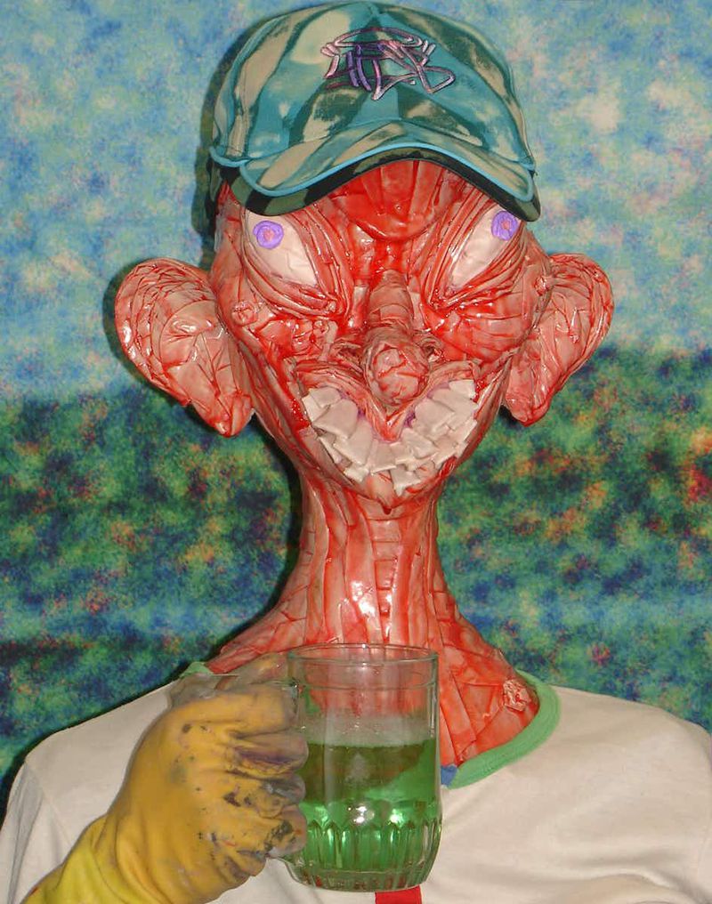 Artistic portrait of a red humanoid figure with a baseball cap, holding a beer mug, against a blurred green and blue backdrop.