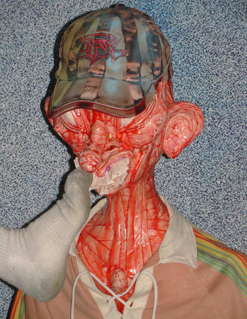 Anatomical human model shows internal muscles and arteries, wearing a baseball cap and clothing, standing in an indoor environment.