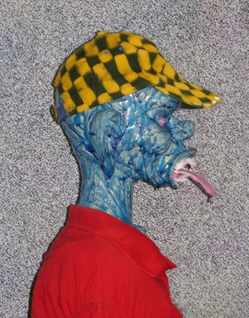 Profile shot of a blue, sculpture-like man with a red shirt and a yellow checkered cap sticking his tongue out.