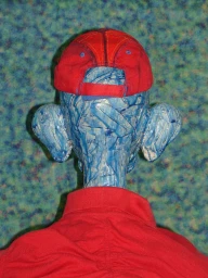 Rear view of a blue textured sculptural head wearing a red baseball cap and red collared shirt against a patterned background.