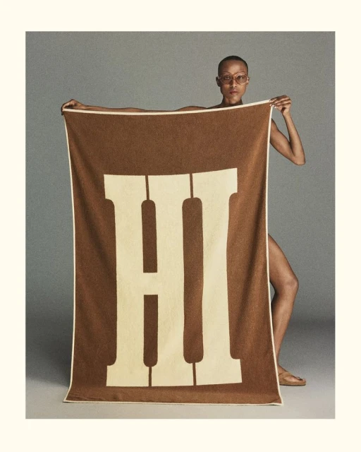 Person holds a brown and tan blanket with a large 'H' design, creating a bold graphic display in a studio setting.