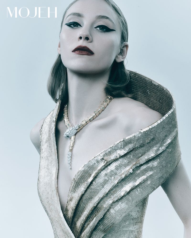 Elegant woman in a gold dress and snake necklace strikes a pose against a bright backdrop, showcasing a high-fashion editorial look.
