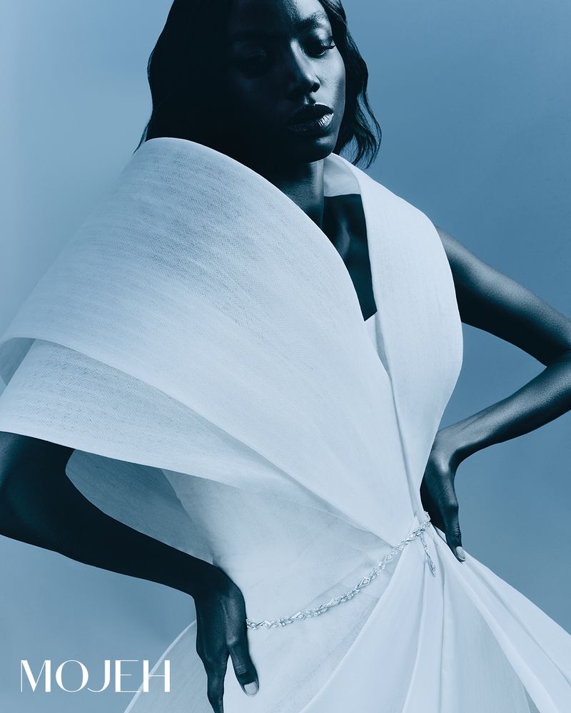 Elegant portrait of a Black woman wearing a white dress with dramatic draping, set against a soft blue background, fashion forward.