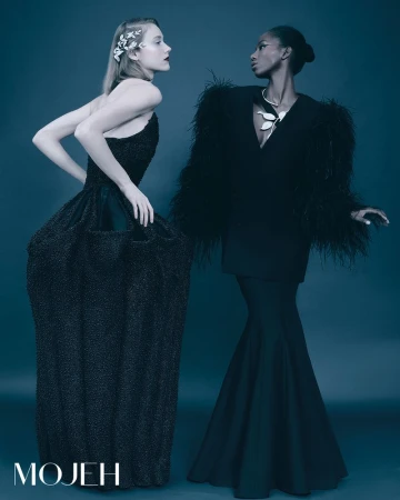 Two fashion models pose in elegant black gowns against a dark cyan background for a formal studio portrait, showcasing high-end fashion.