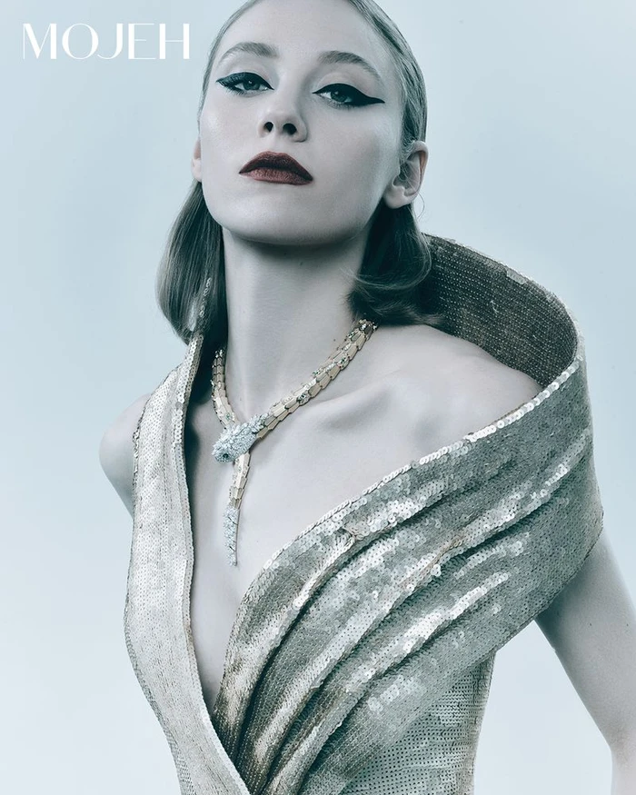 Model wearing a gold sequined dress and serpentine necklace against a plain grey backdrop for Mojeh Magazine