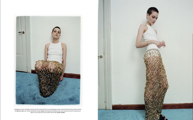 Fashion editorial photo showcasing a woman in a white top and gold skirt posing in front of a white wall with a blue floor.