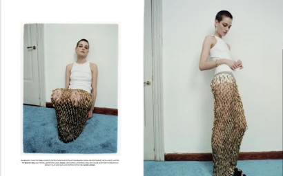 Model with short hair wearing a white tank top and metallic mesh skirt seated on blue carpet against a white wall.