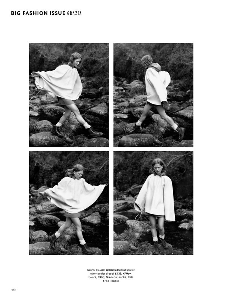 Black and white fashion photo showcases a young adult woman in a light-colored poncho stepping across rocks outdoors in a grayscale outdoor scene.