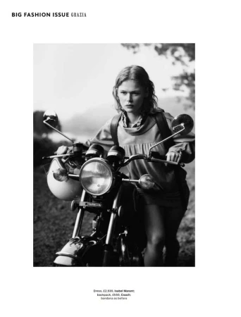 A woman poses with a vintage motorcycle on a rural road, wearing a mini-dress and backpack in a black and white fashion editorial.