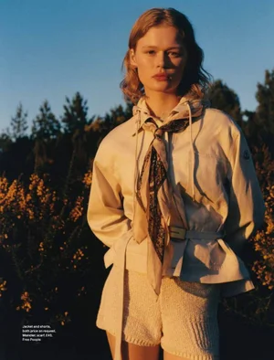 Model Naja Kirk in a cream belted jacket and shorts with a patterned neckscarf outdoors at sunset for Grazia UK