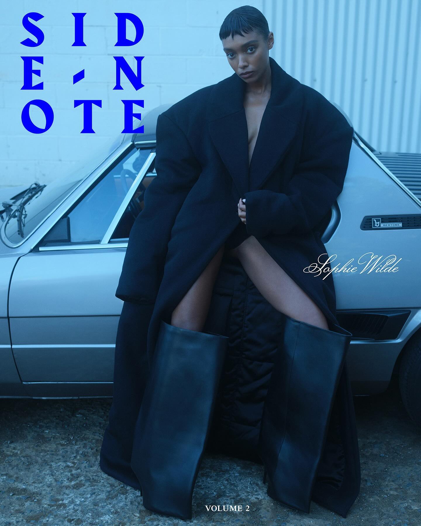 A person poses next to a car wearing a dark, oversized coat and boots, with blue-toned lighting and fashion magazine-style text overlay.