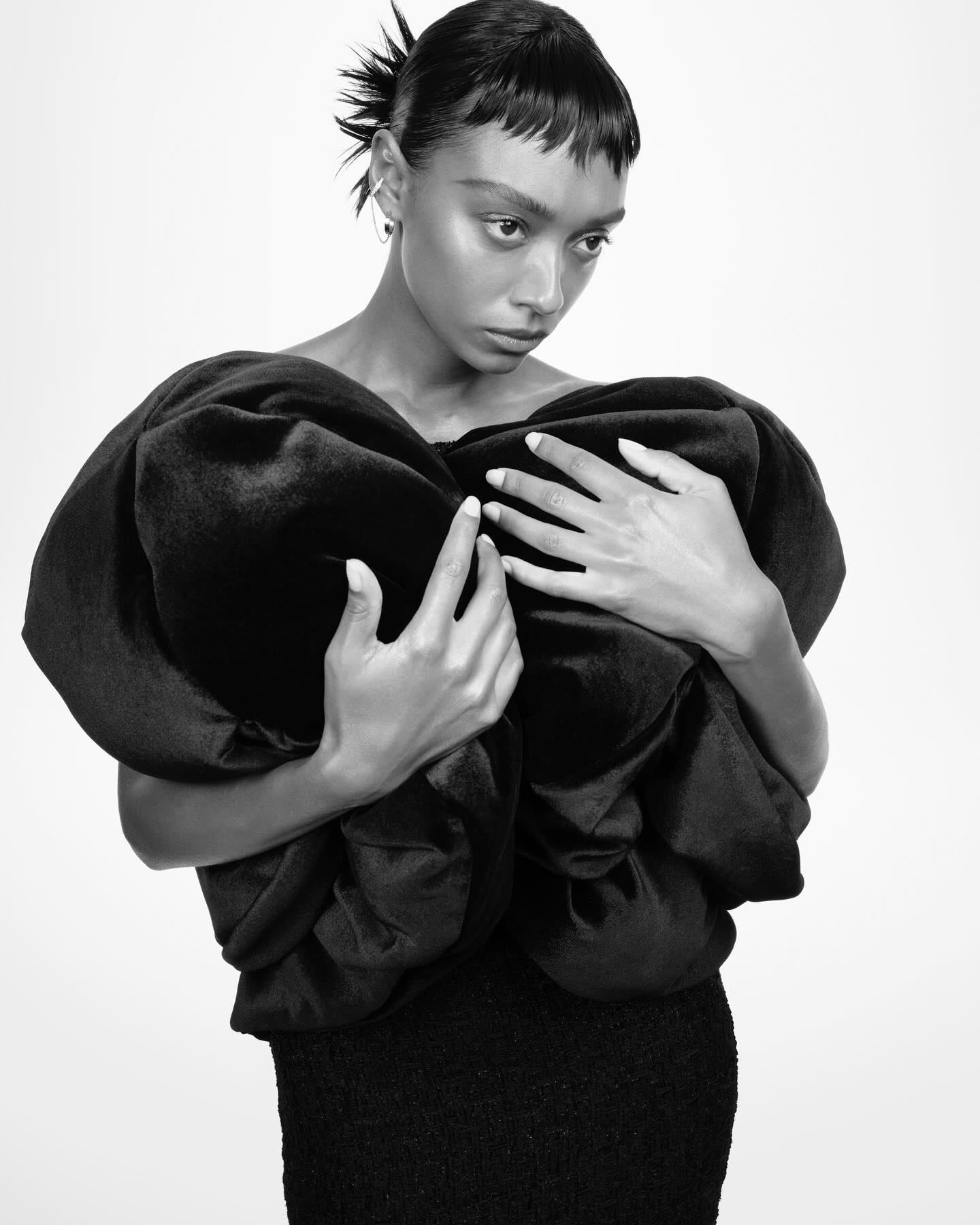 Monochrome portrait of a woman holding sculpted black fabric against a white studio background.