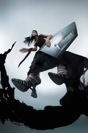 Fashionable Asian woman poses with a Mercedes car part, wearing a black dress and patterned shoes in a studio setting with soft lighting.
