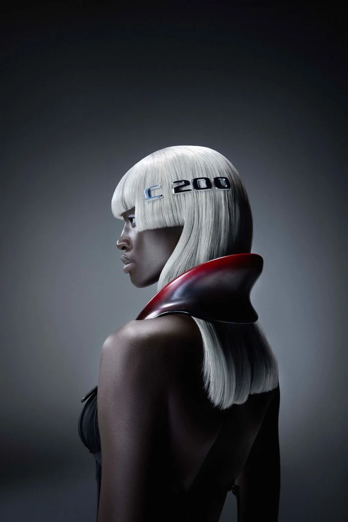 Black woman with white bob hair wearing a high collar red accessory against dark background