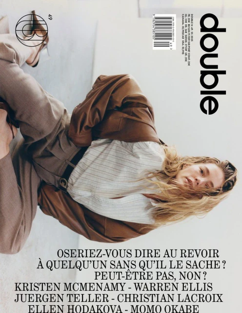 Magazine cover featuring a reclining woman with long blonde hair, wearing a brown suit and white striped shirt, against a light backdrop.