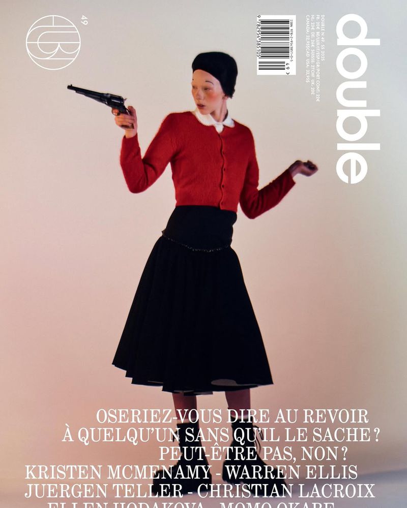 Magazine cover featuring Kristen McMenamy in red sweater and black skirt, holding a gun in a studio setting with text overlay.