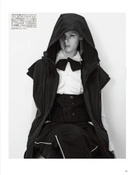 Model in dark hooded vest and white collared shirt with a black bow tie against a white background