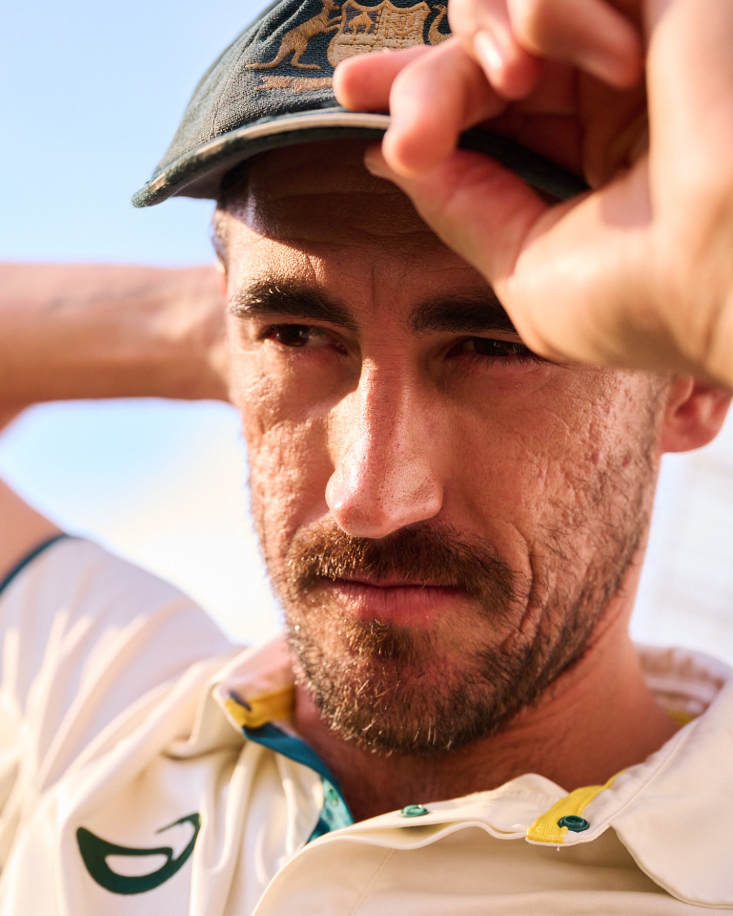 Close-up of a fair-skinned adult male wearing a green and yellow baseball cap and white collared shirt against a blue sky backdrop.