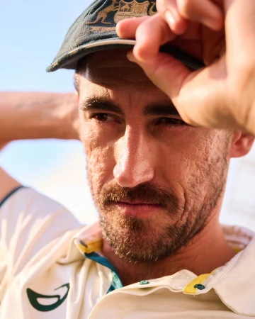 Close-up of a fair-skinned adult male wearing a green and yellow baseball cap and white collared shirt against a blue sky backdrop.