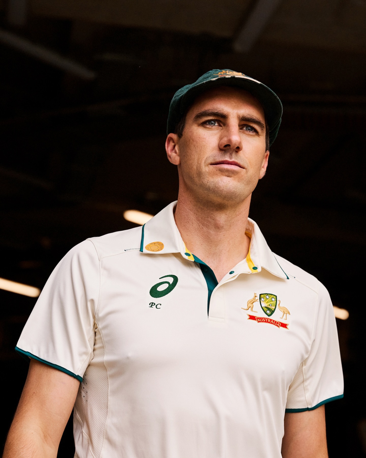 Close-up of a cricket player wearing a cream-colored uniform and a cap, standing in front of a dark background. Sports and athletics.