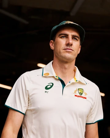 Close-up of a cricket player wearing a cream-colored uniform and a cap, standing in front of a dark background. Sports and athletics.