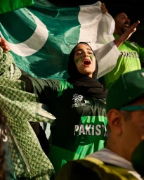 Cricket fans cheering in green jerseys waving a large Pakistani flag at a sports stadium