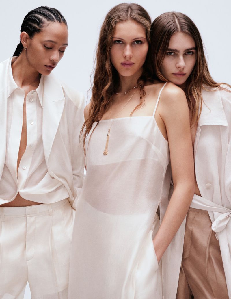 Three women in light-colored apparel pose in a studio, lit with even, neutral lighting, for a fashion editorial; the outfits are coordinated.