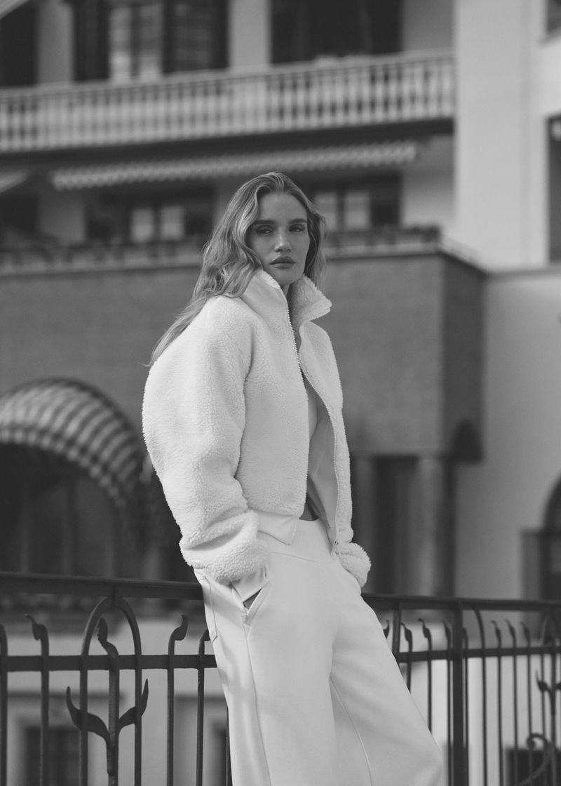 Monochrome portrait of a woman in a white jacket and trousers against a building with iron railing.