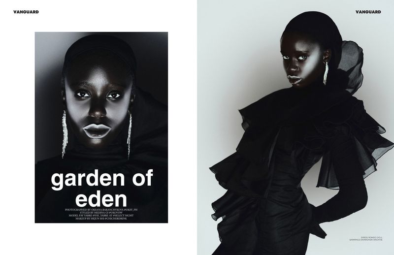 Fashion editorial shot of a Black female model wearing a dark dress and jewelry, posing in front of a gradient studio background.