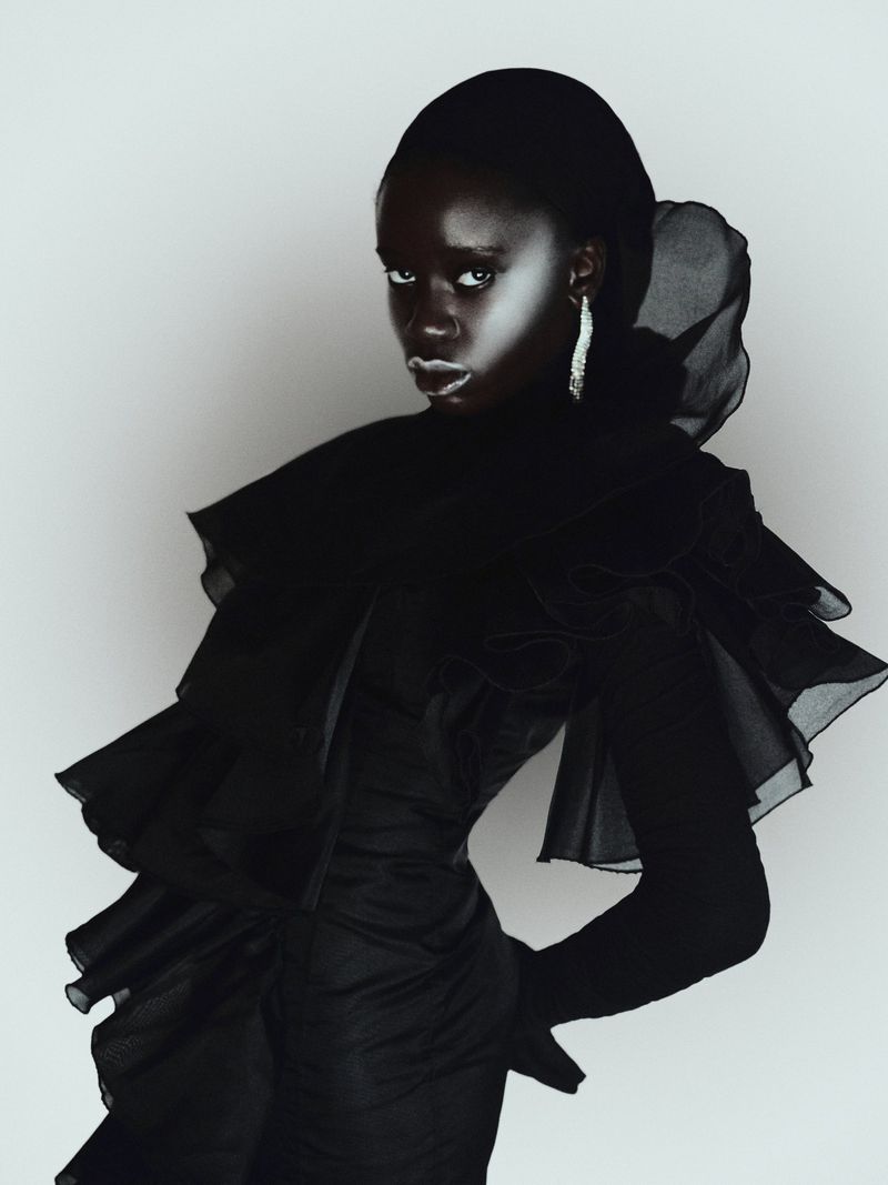 Fashion portrait of an adult African woman with dark skin in a black dress with ruffles, statement earrings, and silver lipstick.
