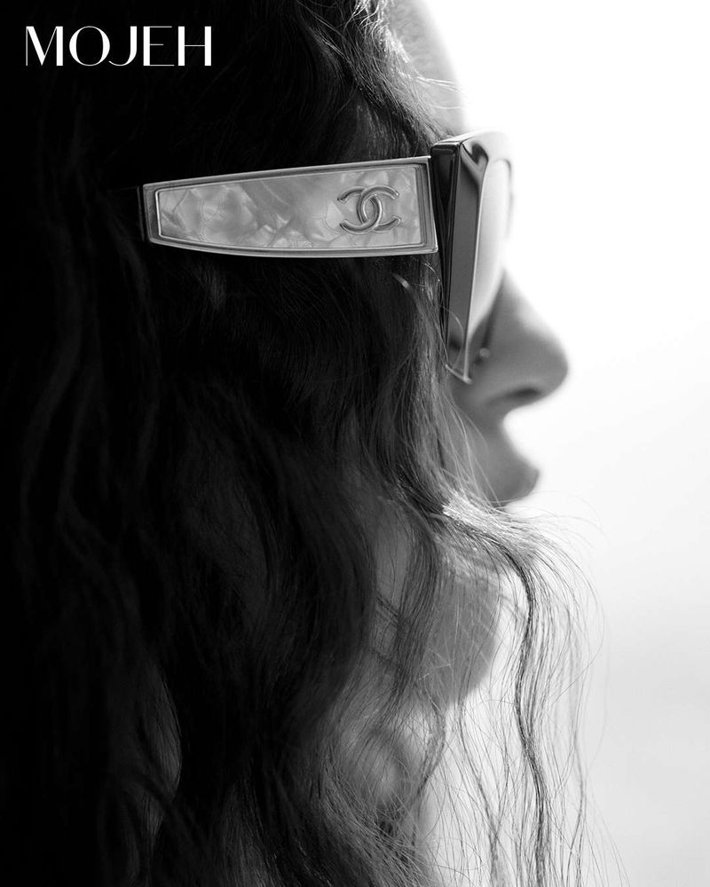 Elegant close-up of a woman's profile featuring stylish Chanel sunglasses, black hair, and a bright, soft-focus background.