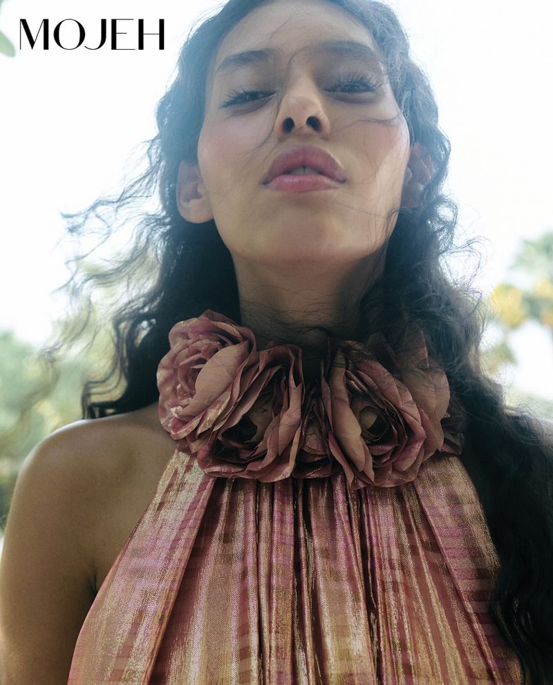 Low angle close-up of model Allana Neiva wearing a shimmering rose halter dress with fabric floral collar rosettes for Mojeh Magazine.
