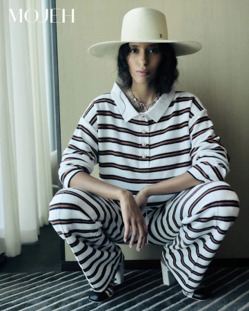 Model crouching wearing a striped polo outfit and wide-brimmed hat in an editorial portrait for Mojeh Magazine.