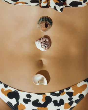 Close-up studio shot of a woman's torso with seashells on her stomach and wearing a patterned bikini top and bottom.