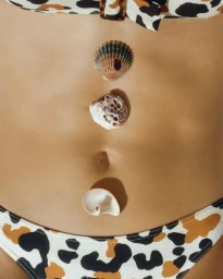 Close-up of model Hilary Rhoda wearing an animal-print bikini with three seashells aligned on her abdomen for Erès SS25.