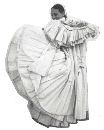 Monochrome portrait of woman in ruffled gown, sleeves, and collar, smiling slightly with eyes downcast, full shot on white backdrop.