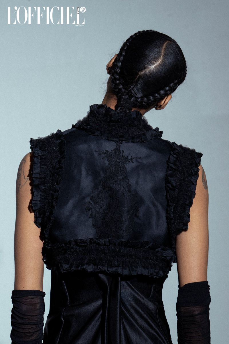Back view of a woman with braided hair, wearing a black ruffled bolero jacket, black dress and sheer gloves, fashion studio shot.