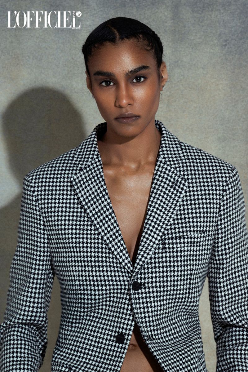 Adult female fashion model poses in a black and white houndstooth blazer looking directly at the camera in a studio setting.