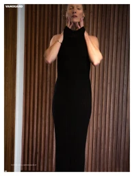 Model wearing a black sleeveless ribbed dress standing against vertical wooden paneling for Vanguard Magazine.