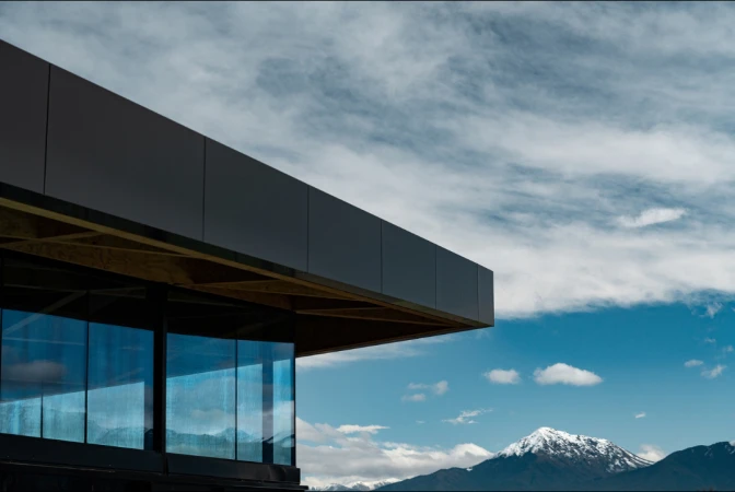 Modern architecture features a sleek, dark building against a backdrop of a blue sky, clouds, and distant snow-capped mountains.