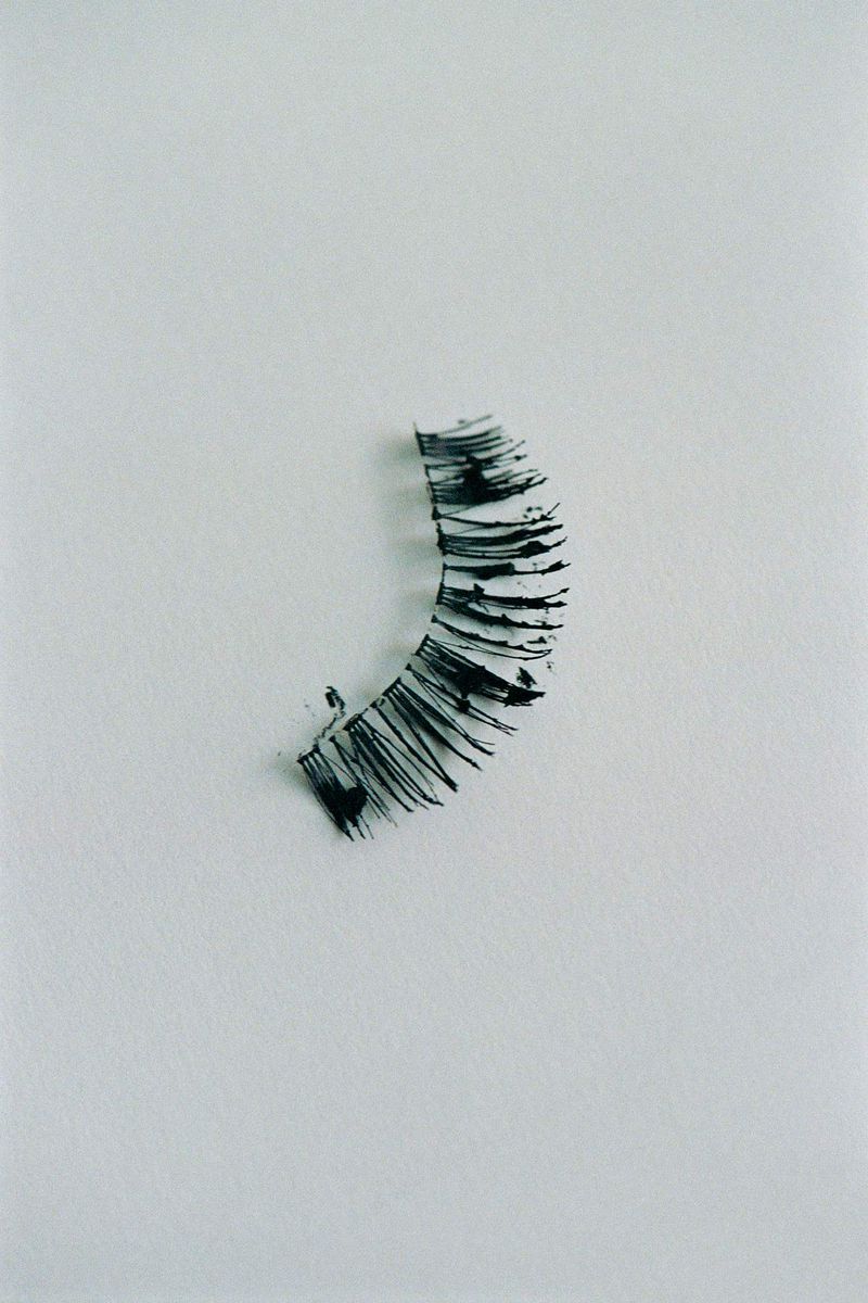 Close-up of a black false eyelash strip on a white surface, showcasing beauty and personal care accessories in a minimalist style.