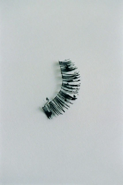 Close-up of a black false eyelash strip on a white surface, showcasing beauty and personal care accessories in a minimalist style.
